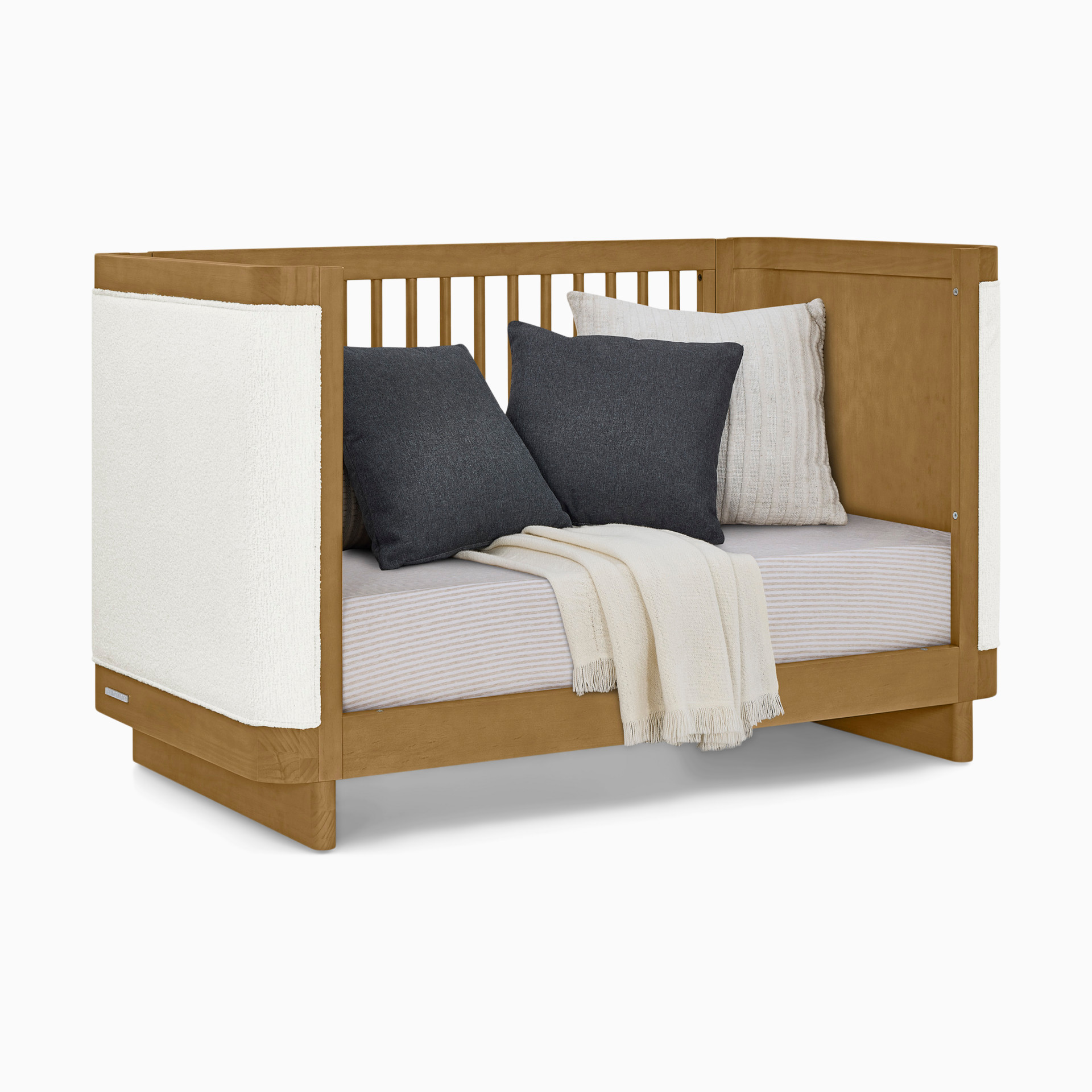 Wooden crib styled as a nursery with various pillows and a blanket.
