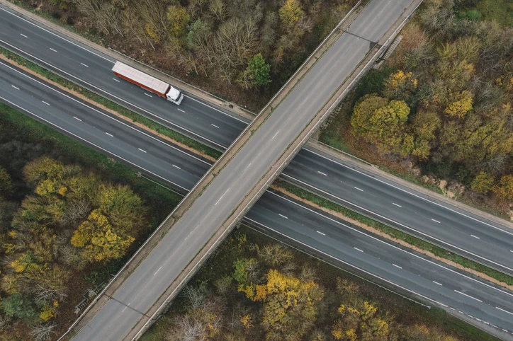 A photo taken above of a lorry driving on an A road. There is a bridge that goes over the road