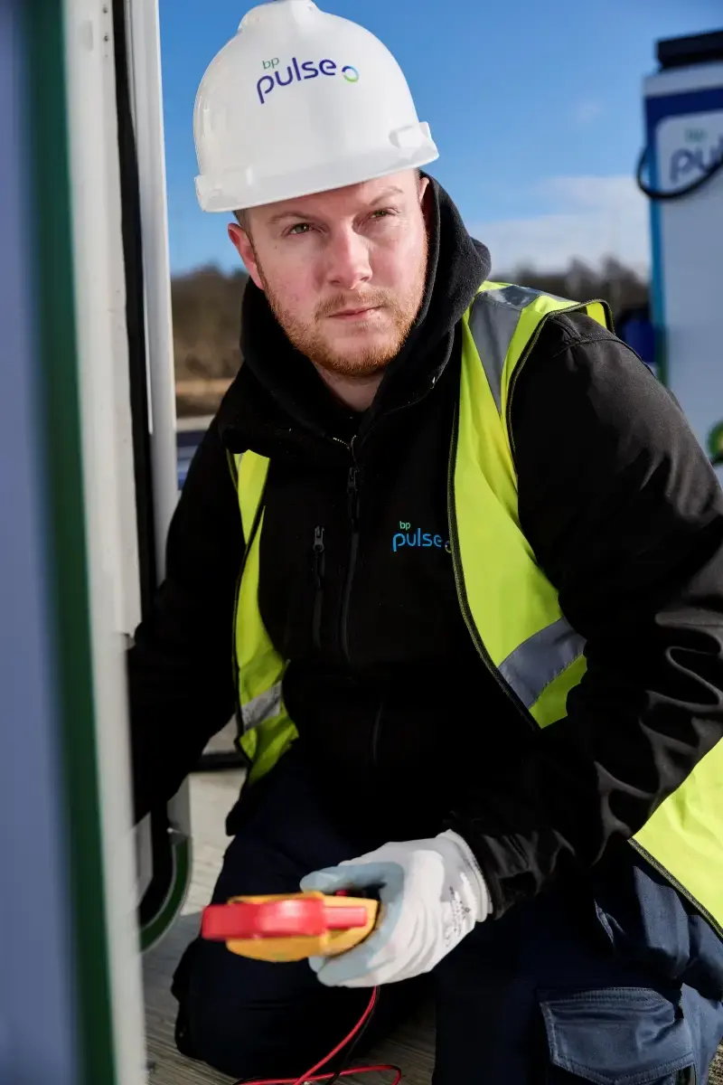 A photo of a man installing a bp pulse ultra-fast charger. He is looking off into the distance wistfully