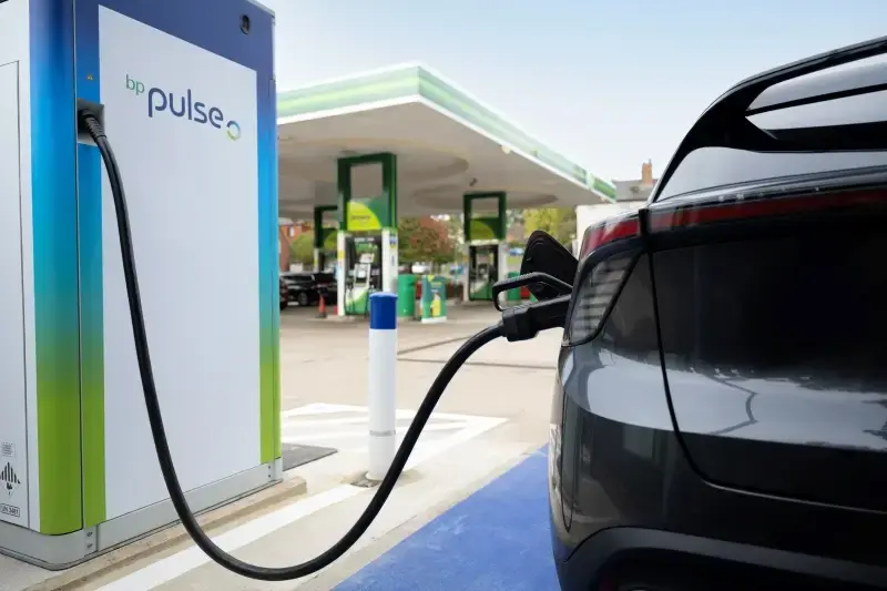 A close up photo of a bp pulse charger in use on a forecourt. It is plugged into a dark car.