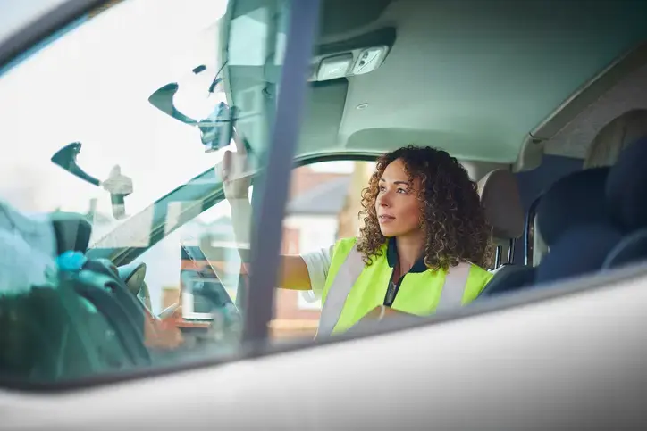 An image of a female fleet driver in a high vis jacket sitting in her van. She is plotting her course on a sat nav