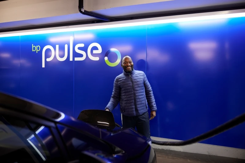 A male Uber driver at the Pimlico Q-Park Gigahub standing by his car and smiling at the camera