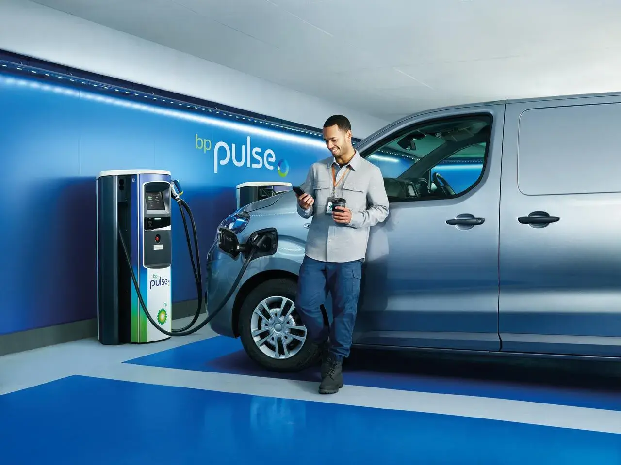 Man checks his phone whilst his grey electric van charges