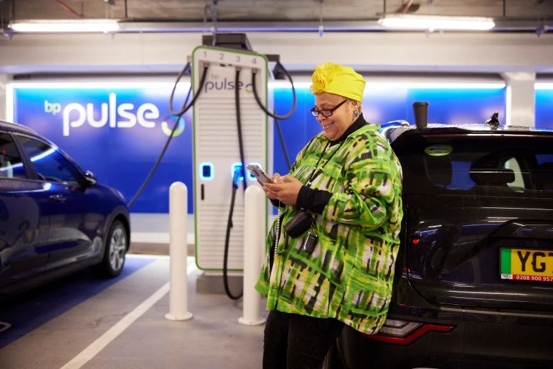 A female Uber driver at the Pimlico Q-Park Gigahub leaning on her car and looking at her phone