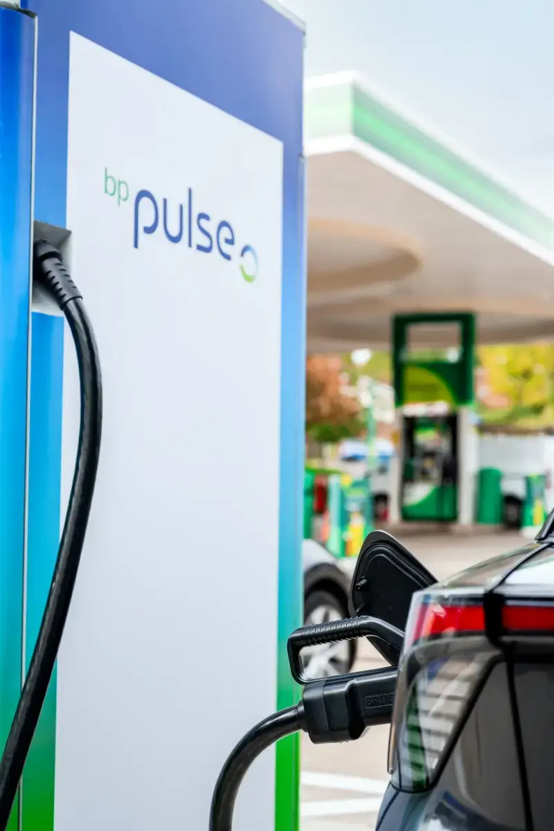 A photo of a bp pulse charger in a forecourt. Its cable is plugged into a car