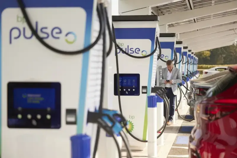 A photo of a man at the NEC Birmingham charging hub. He is surrounded by bp pulse chargers and is looking down at his phone.