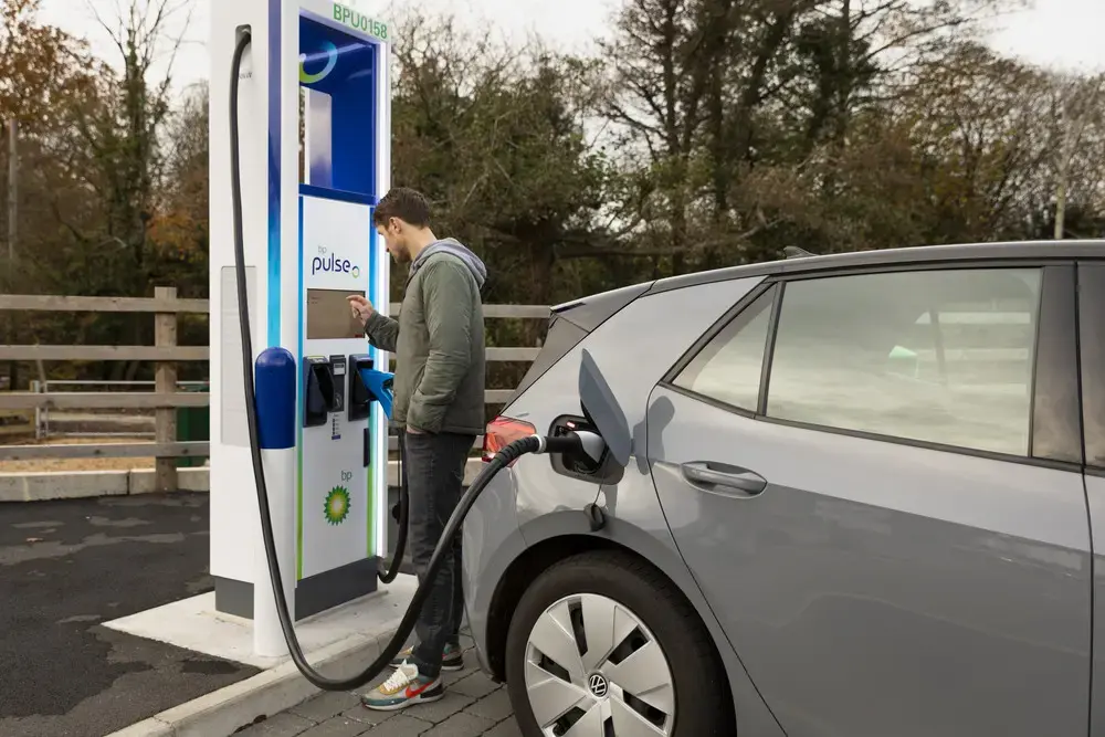 A photo of a man charging his car using an ultra-fast charger at a new bp pulse forecourt