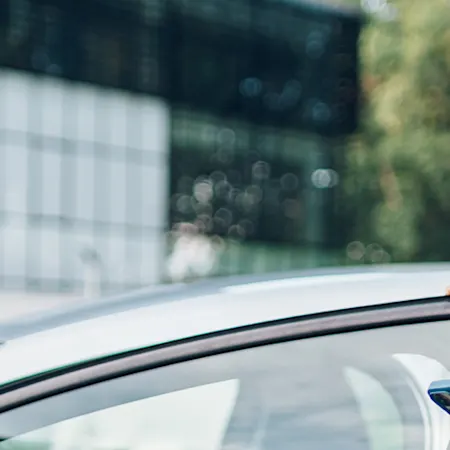 Frau steht am Auto uns schaut nach News der Contipark auf ihrem Smartphone