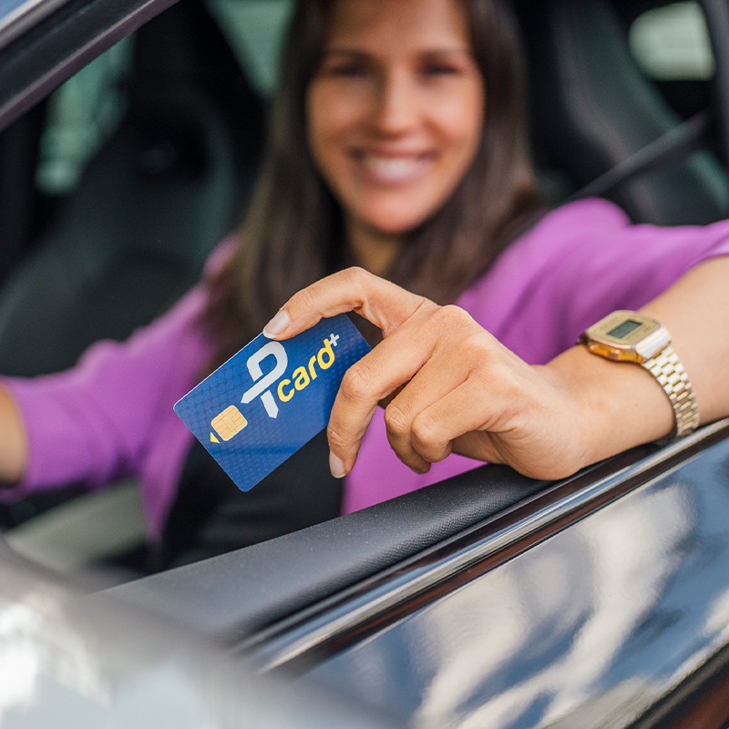 junge Frau im Auto am Steuer hält die Kundenkarte Pcard in der Hand aus dem Fenster
