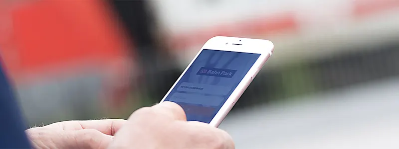 Mann mit Smartphone in der Hand steht vor einem Zug