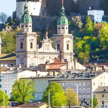 Parken in Salzburg: Panoramablick auf die Festung Hohensalzburg die auf einem Berg steht und von der Stadt Salzburg umgeben ist.