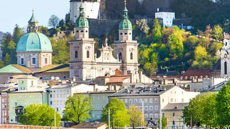Parken in Salzburg: Panoramablick auf die Festung Hohensalzburg die auf einem Berg steht und von der Stadt Salzburg umgeben ist.