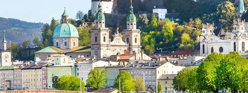 Parken in Salzburg: Panoramablick auf die Festung Hohensalzburg die auf einem Berg steht und von der Stadt Salzburg umgeben ist.