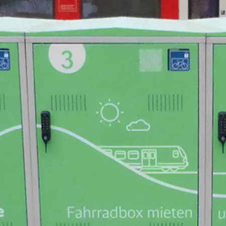 Fahrradboxen vor einem Bahnhof mit Zug