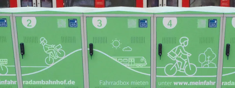 Fahrradboxen vor einem Bahnhof mit Zug