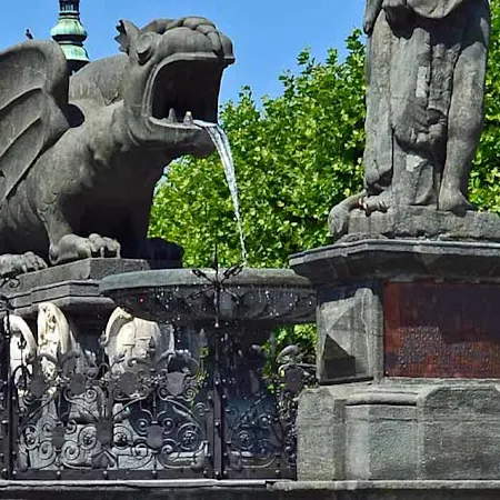 Parken in Klagenfurt: Im Vordergrund ist der Drachenbrunnen zu sehen im Hintergrund befindet sich das Rathaus der Stadt Klagenfurt.