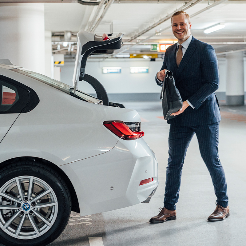 junger Mann in der Tiefgarage stellt seine Aktentasche in den geöffneten Kofferraum seines Autos