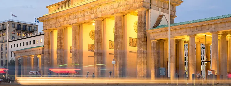 nächtliche, beleuchtete Straße auf das Berliner Brandenburger Tor hinführend