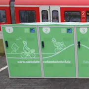 Fahrradboxen vor einem Bahnhof mit Zug