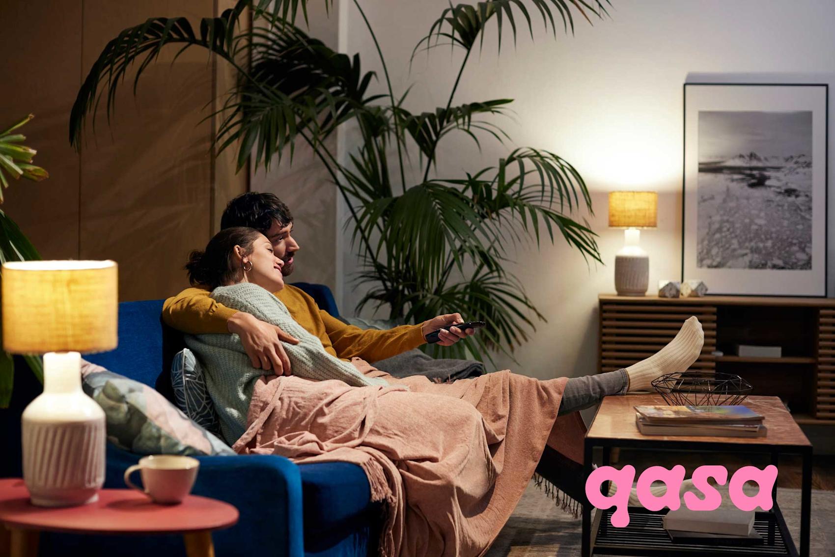 Par håller om varandra i soffa i vardagsrum. Rosa qasa logo över bil