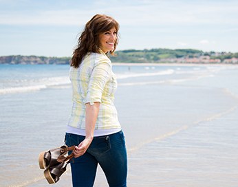 Eine lächelnde Frau, die am Meeresufer entlang spaziert.