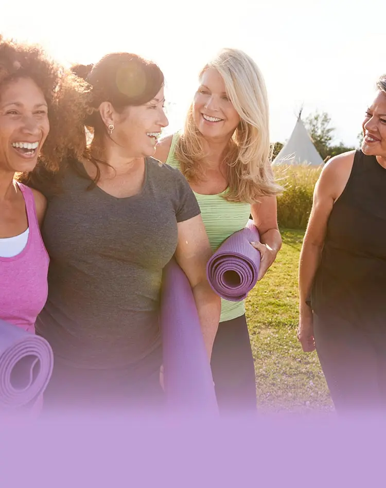 Drei lächelnde, sportlich gekleidete Frauen halten ihre Trainingsmatten