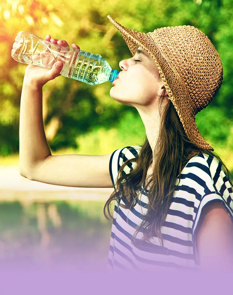 Eine junge Frau mit einem Hut trinkt Wasser aus einer Flasche