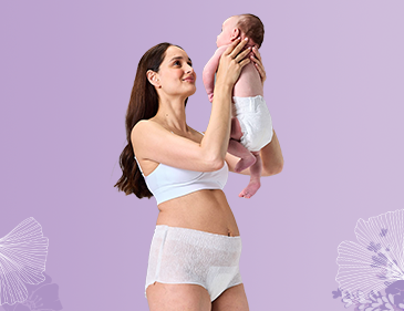 Eine Frau in Wochenbettunterwäsche hält ein neugeborenes Baby in ihren Armen.