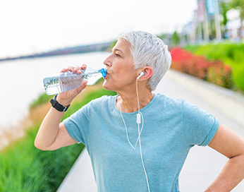 Eine Frau mit In-Ear Kopfhörern trinkt Wasser, während sie Sport treibt