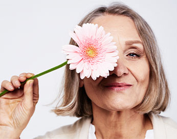 Eine Frau mittleren Alters bedeckt ihr Auge mit rosa Blume