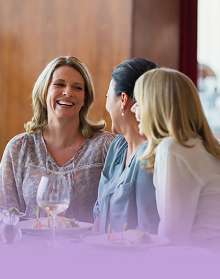 Drei lächelnde Frauen unterhalten sich bei einem Glas Wein