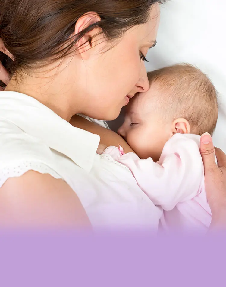 Eine liegende Frau umarmt ihr Baby und küsst es auf die Stirn