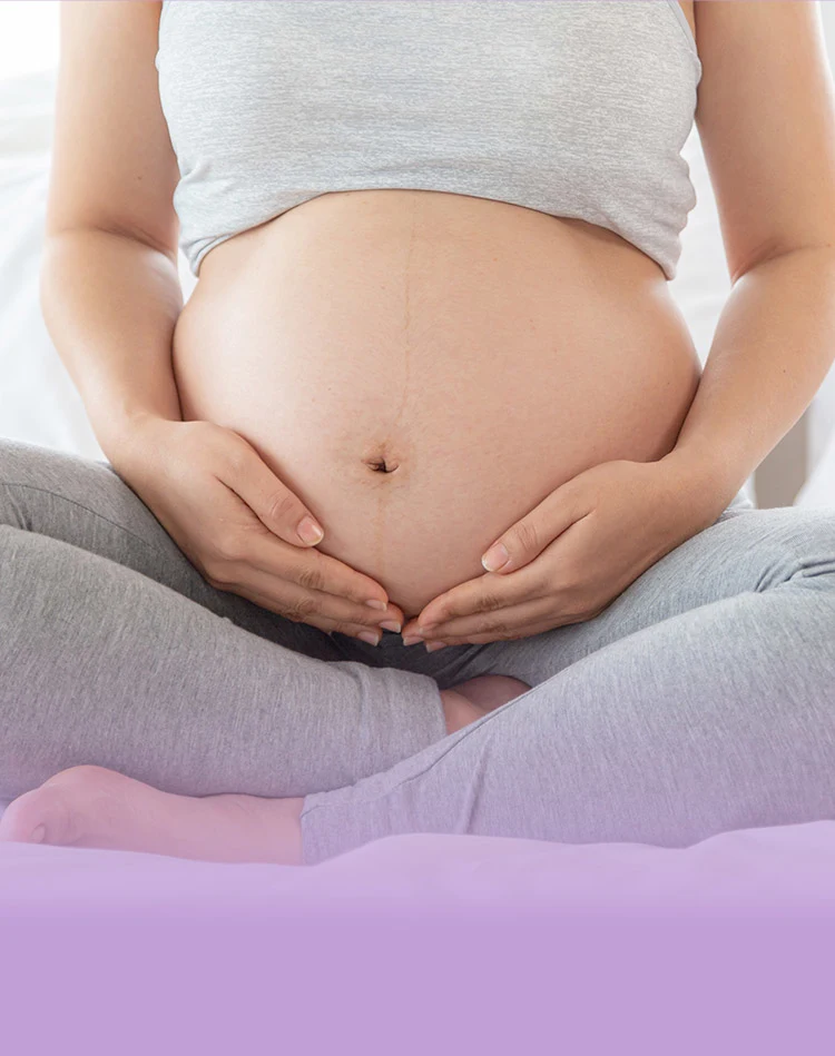Eine Frau sitzt im Schneidersitz und stützt ihren entblößten Bauch zärtlich mit beiden Händen