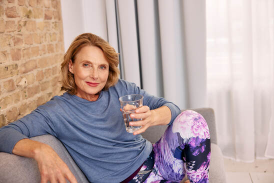 Lächelnde Frau mittleren Alters hält Glas Wasser in der Hand