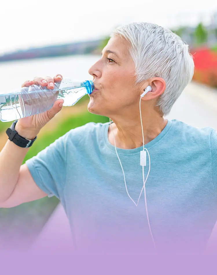 Eine Frau mit In-Ear Kopfhörern trinkt Wasser, während sie Sport treibt