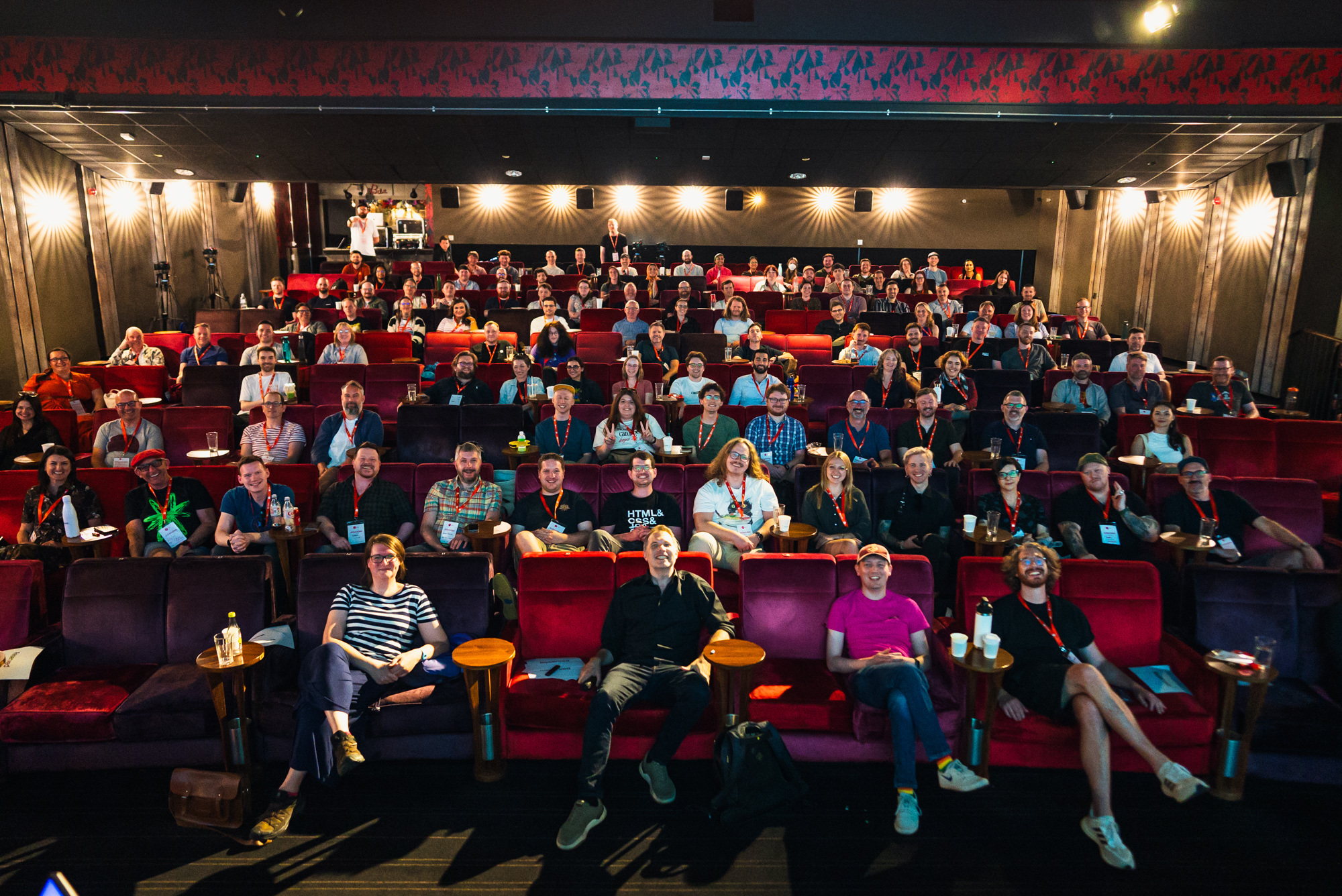 The conference attendees are photographed from the stage with the house lights on. They are sitting on red velvet, very comfortable chairs, as this is a cinema. Everyone looks energised yet calm after a very good conference day.