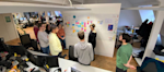 A wide angle view of Salma and a tech team in an open plan office
