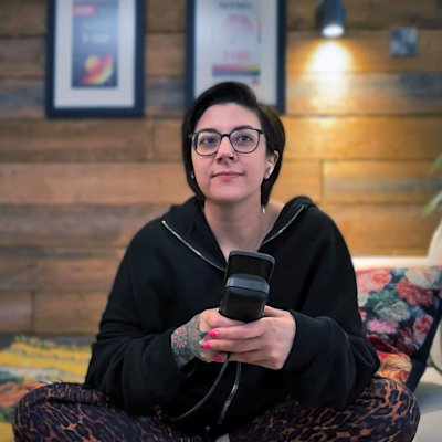 Salma sitting cross legged on a sofa, holding a microphone, looking up into the right of the space.