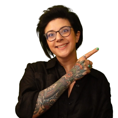 Salma is looking at you, with a rather large smile. She's pointing across herself up to her left, with a very tatooed arm. She's wearing a black shirt and black rimmed glasses.
