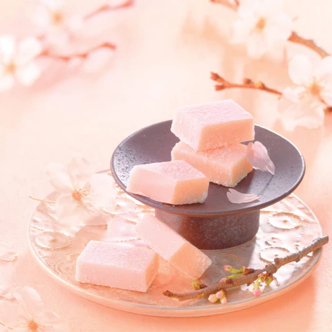 Pink, rectangular chocolates sitting on a dish, surrounded by small branches of sakura blossoms