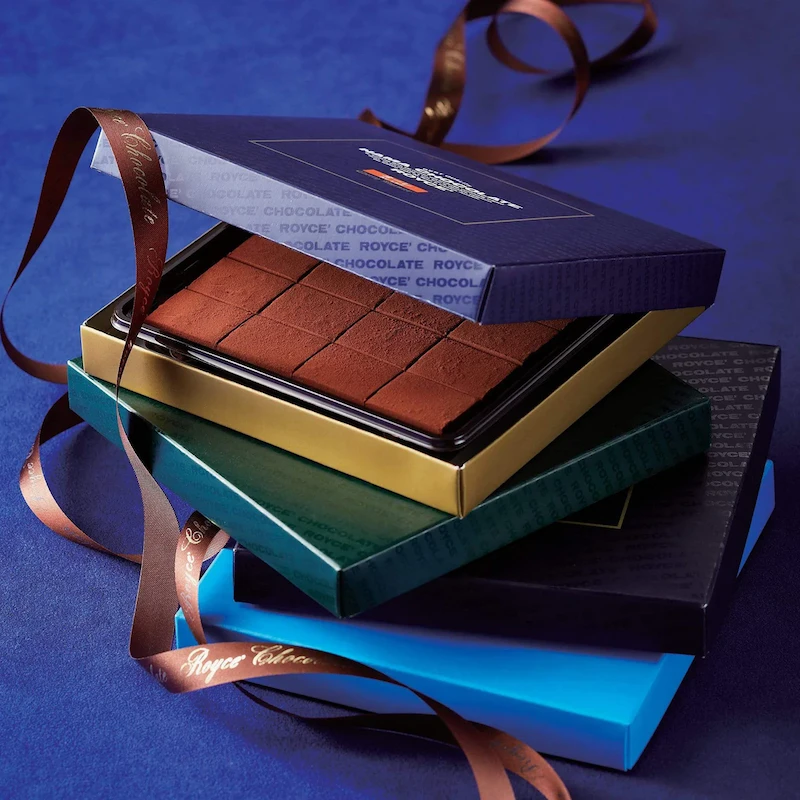 A box of uniform, rectangular chocolates perched on top of a stack of other chocolate boxes