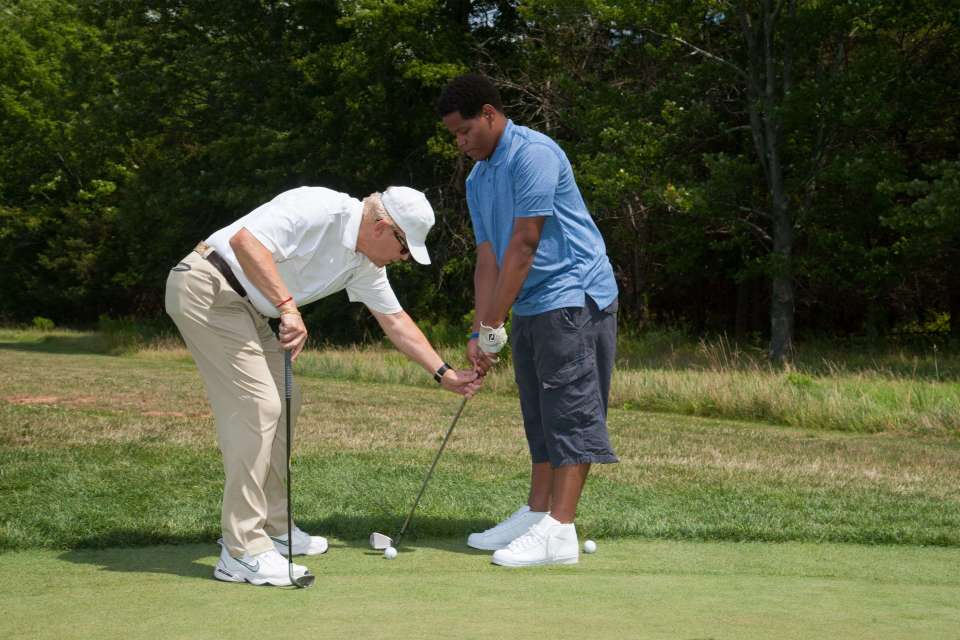 Golf professional giving a private golf lesson on a driving range on how to hit a ball.