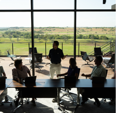 Image of people talking at a long desk, with a golf course in the distance