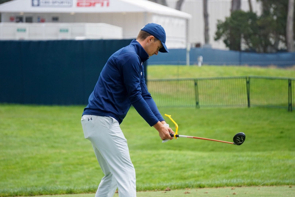 Professional golfer improving his golf swing with a  teaching aid on the golf course.
