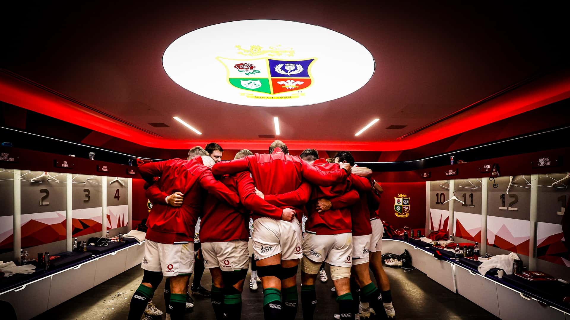 Lions Mens Squad huddled in the dressing room with a crest above them.
