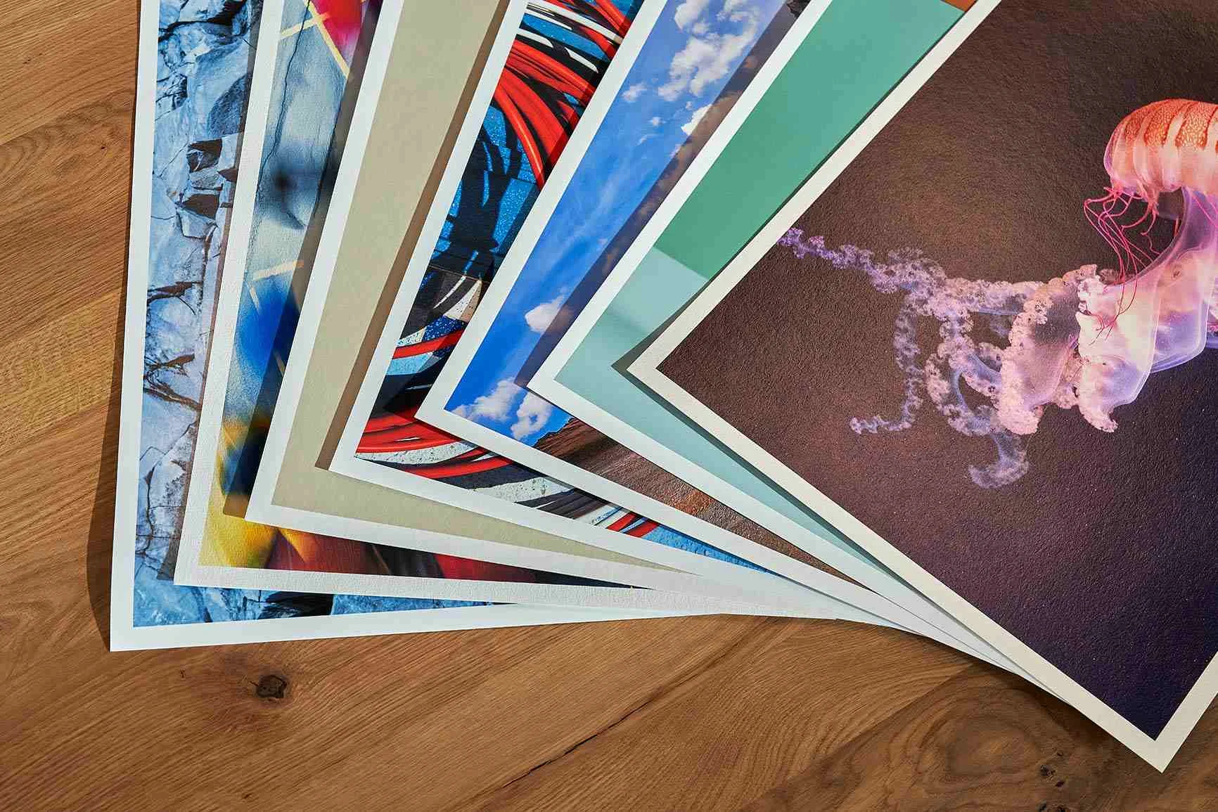 Mehrere Fine Art Prints mit verschiedenen Motiven liegen auf einem Holztisch übereinander.