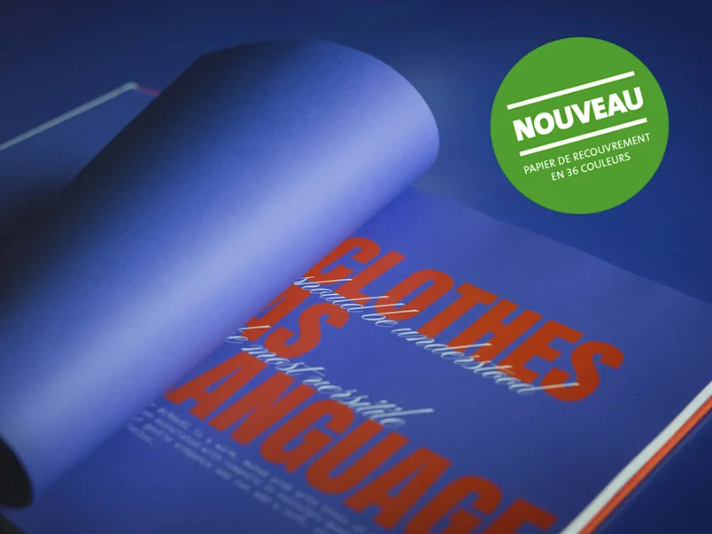 Page de livre ouverte avec texte orange "CLOTHES IS LANGUAGE" sur fond bleu et autocollant vert avec texte blanc "NOUVEAU PAPIER DE RECOUVREMENT EN 36 COULEURS"