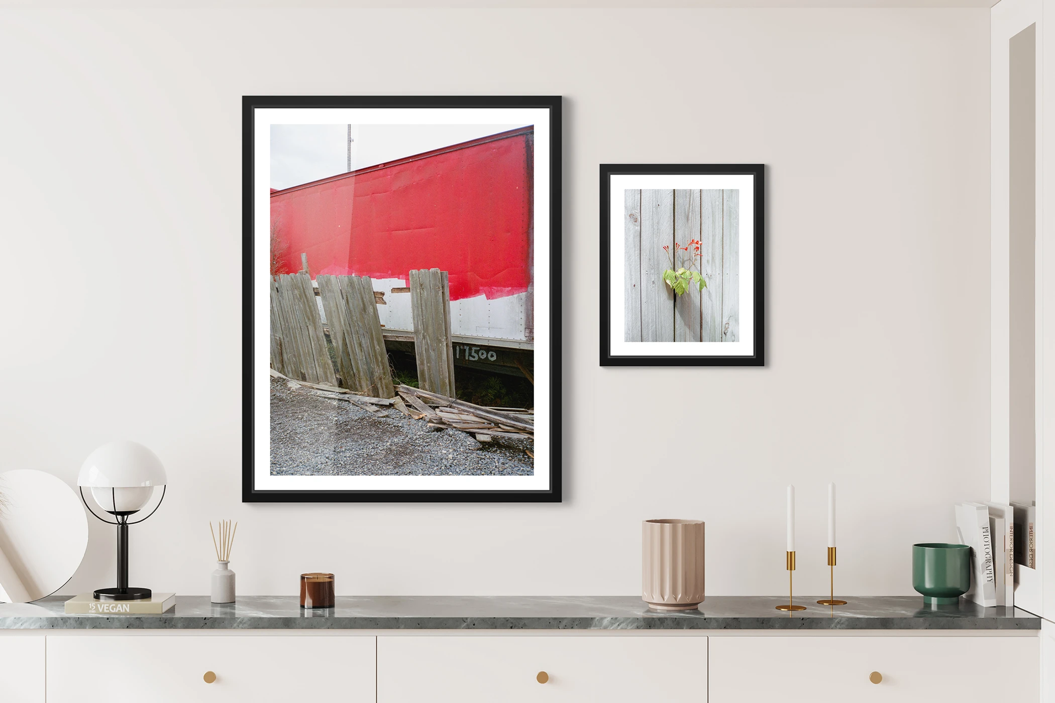 On the left a broken wood fence in front of a train which is partially painted red and on the right a plant with small red flowers peeking through a dense wooden fence.