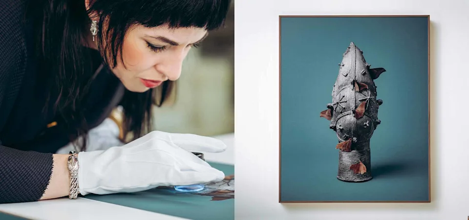Une personne portant des gants blancs manipule une grande photographie encadrée en bois clair. L'œuvre représente un artefact en bronze orné de papillons marrons sur un fond bleu-vert uni. Le profil de la personne apparaît dans le coin inférieur gauche, tandis qu'un second cadre identique est visible de manière floue à droite. La scène évoque la préparation d'une exposition artistique.