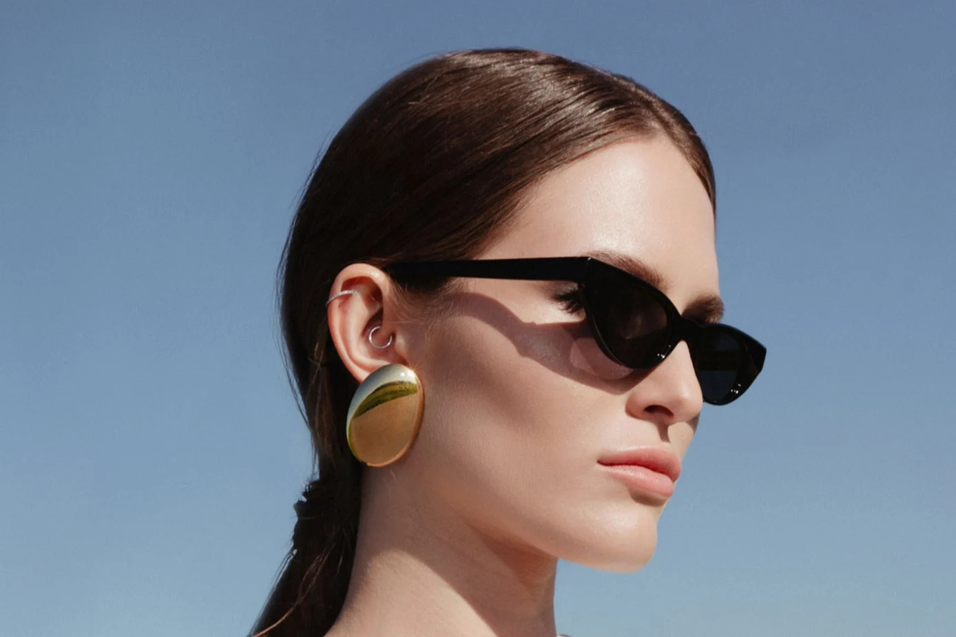 Portrait of a woman with her hair tied back, set against a clear sky in daylight.
